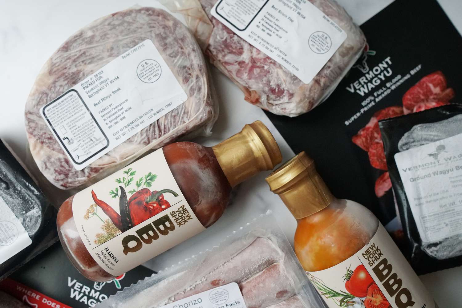 Several frozen pieces of meat and two bottles of barbecue sauce on a marble surface