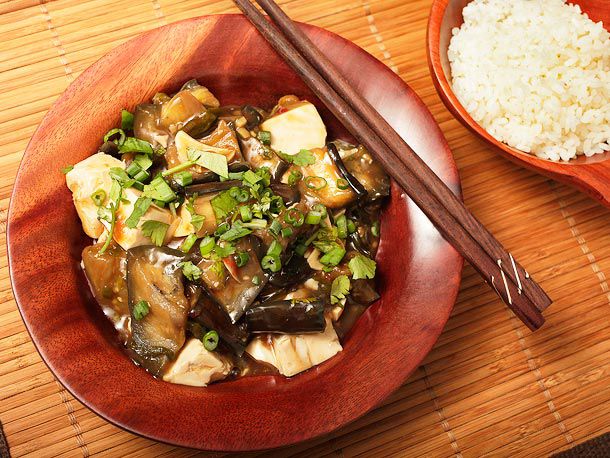 Overhead shot of braised eggplant with tofu, garnished with chopped scallions with a side of steamed white rice.