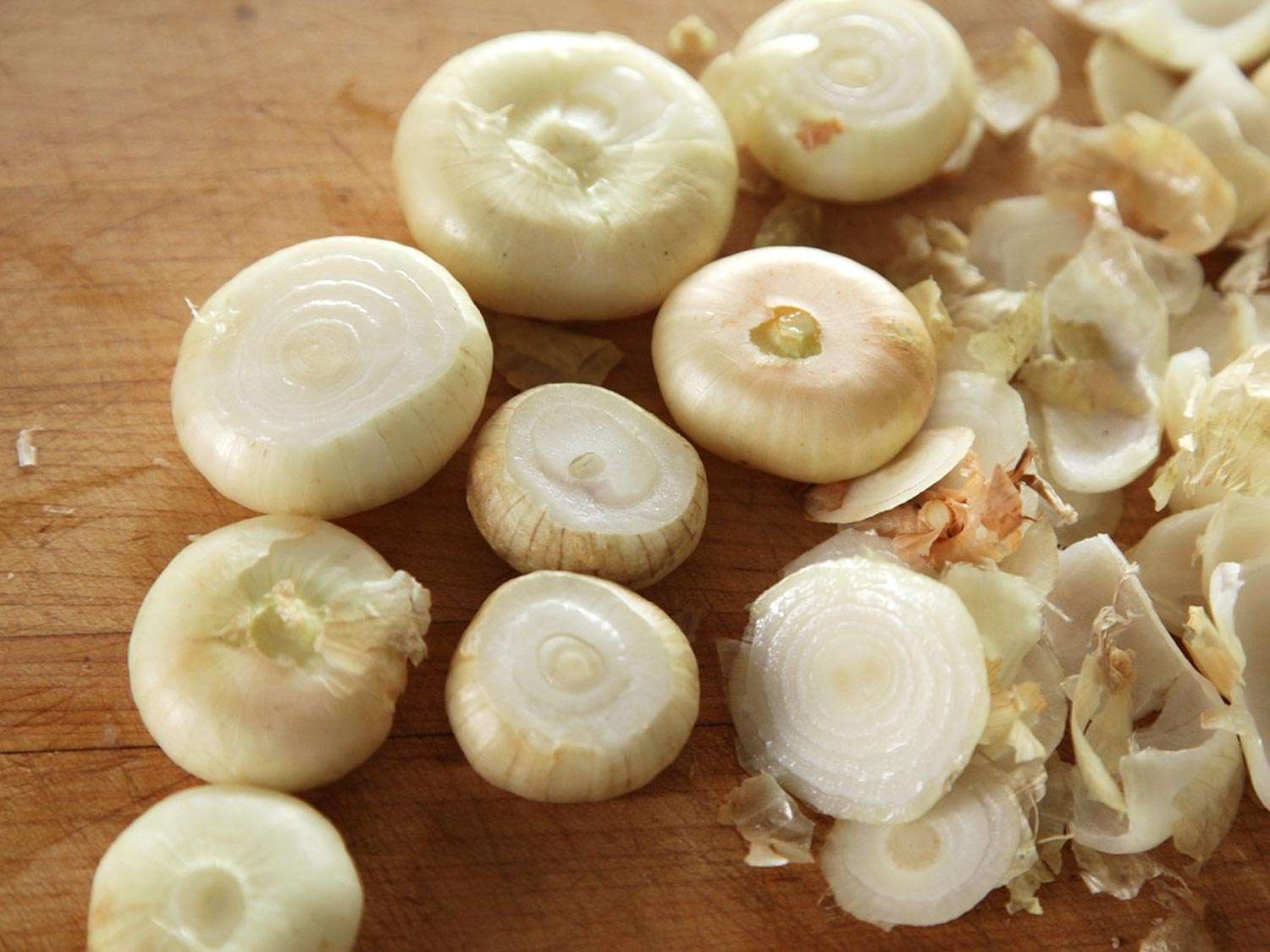 Cutting off the tops and bottoms of cipollini onions, and peeling them.