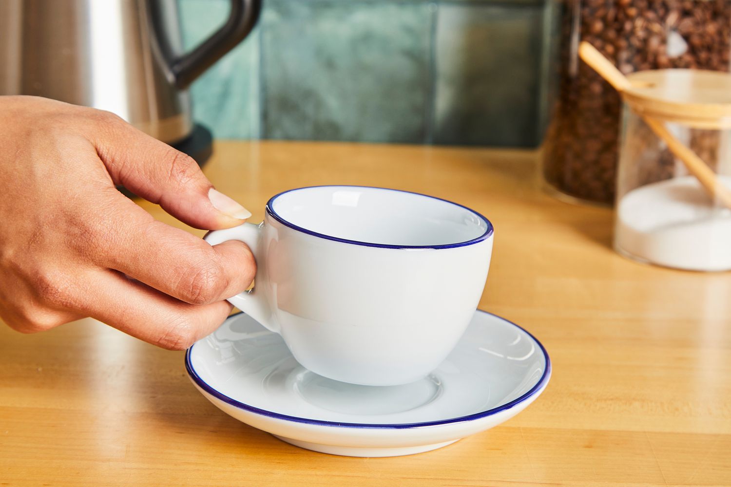 A person picking up a coffee mug off of a saucer.