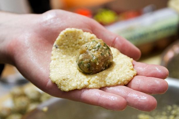 A hand holding a flattened portion of matzo meal batter with a meatball on top