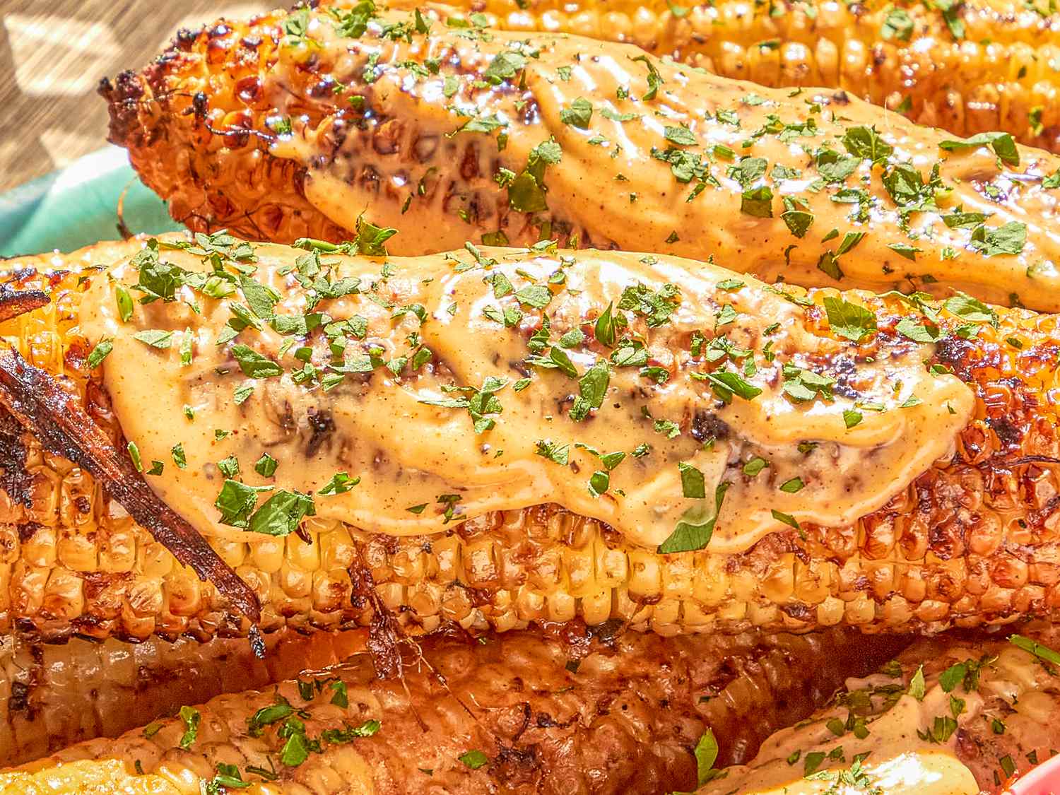 Grilled corn topped with sauce and garnished with herbs