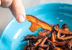 A person holds a piece of cooked mushroom over a blue bowl containing more cooked mushroom pieces