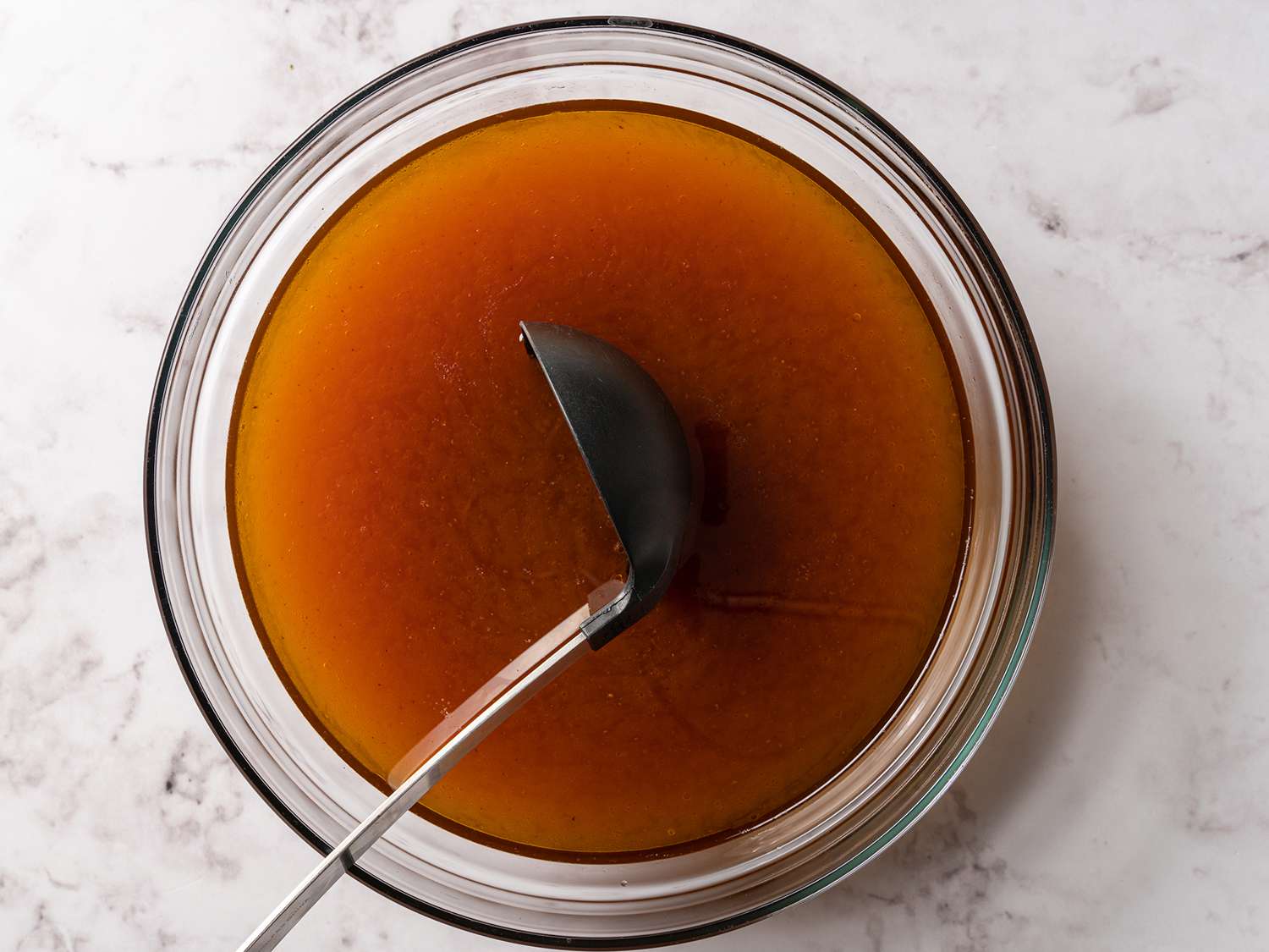 A ladle skimming the top of the beef stock