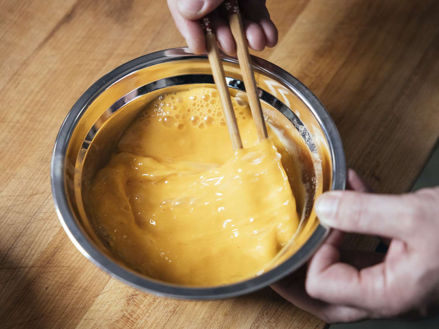 Cornstarch and eggs being whisked together in a metallic bowl with chopsticks.