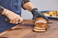 A person cuts meat with the Wüsthof Classic 9 Inch Hollow Edge Carving Knife