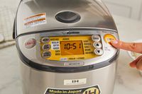 A person pressing start on the Zojirushi rice cooker.