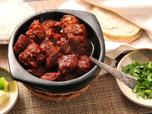 A small bowl of carne adovada with cilantro and tortillas next to it.