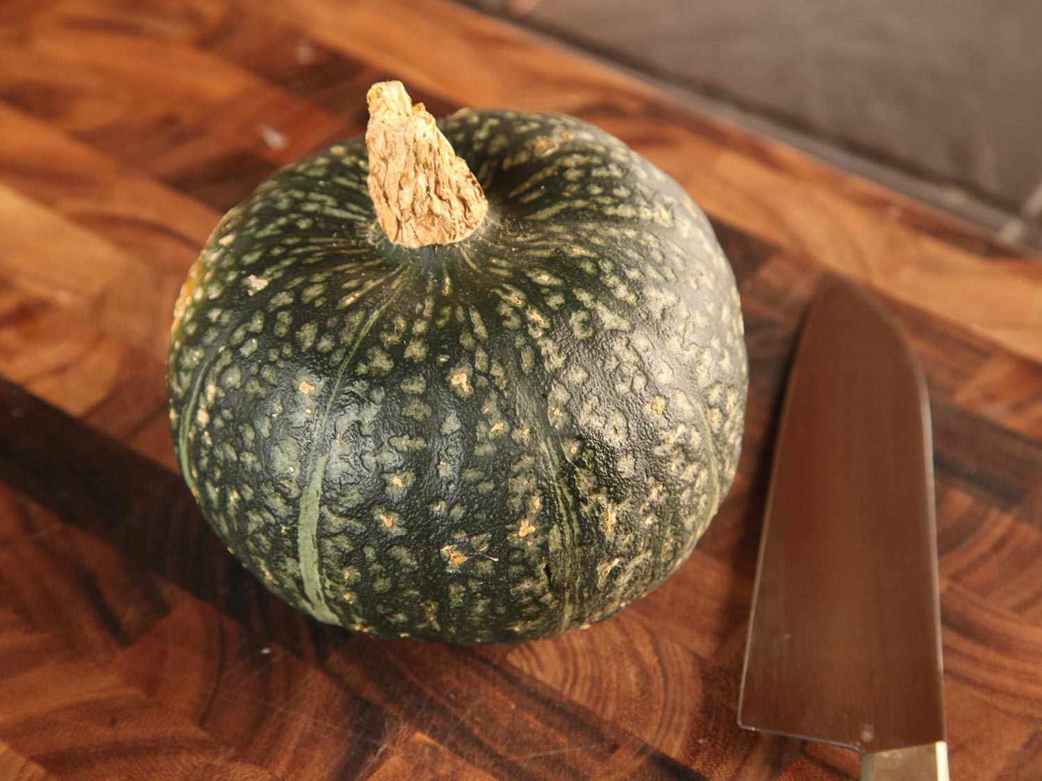 Whole kabocha squash on a wooden cutting board.