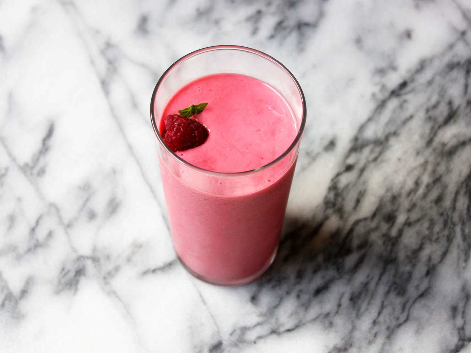 A glass of raspberry, mint, and kefir smoothie on a marble surface.