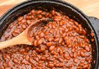 A crock of barbecue beans being stirred with a wooden spoon.