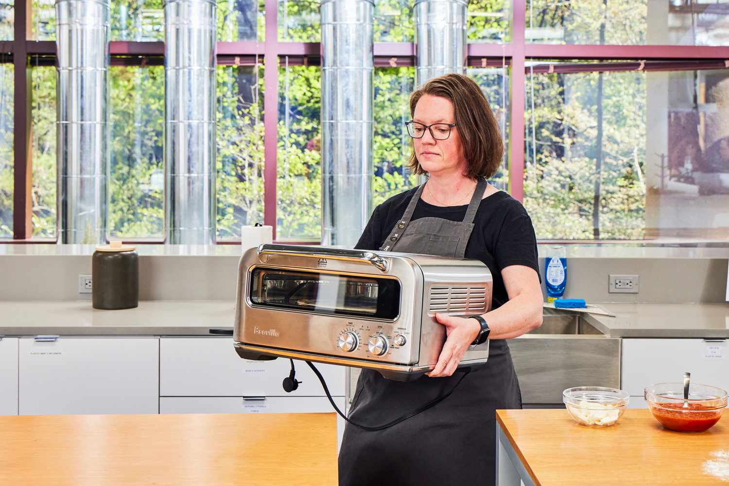 A person lifts the Breville Smart Oven Pizzaiolo Pizza Oven