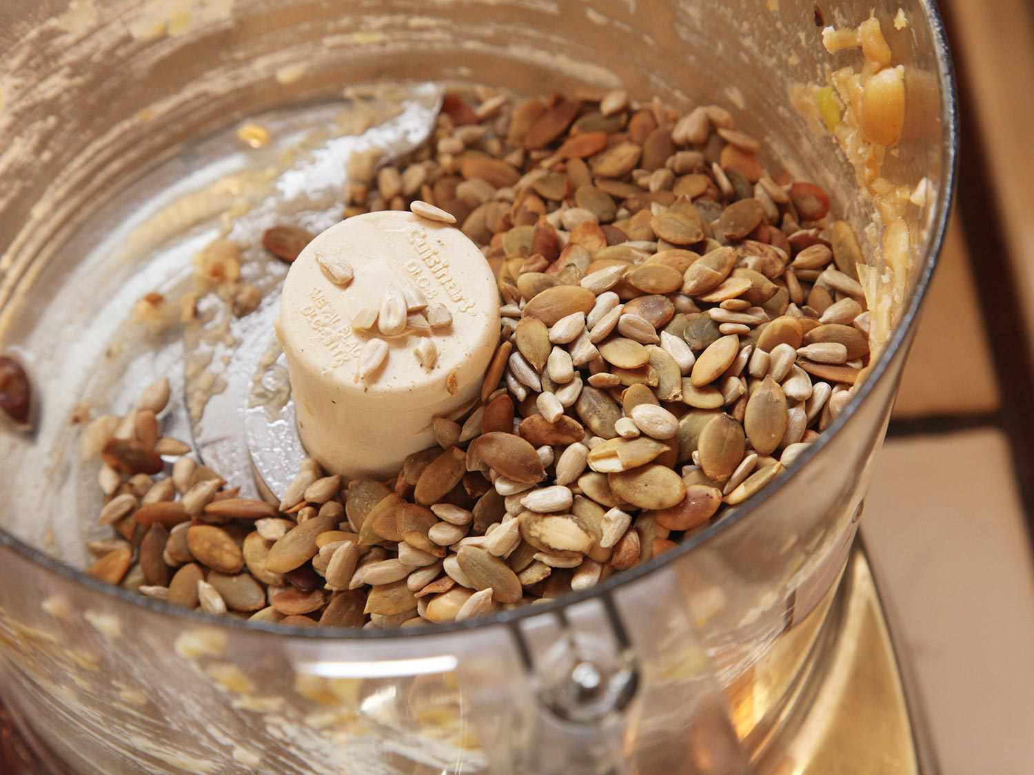 Toasted sunflower seeds and pepitas in the bowl of a food processor.