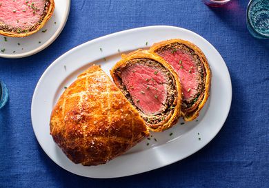 Beef Wellington on an oval white ceramic plate, with two slices of Wellington on the right hand side of the plate.