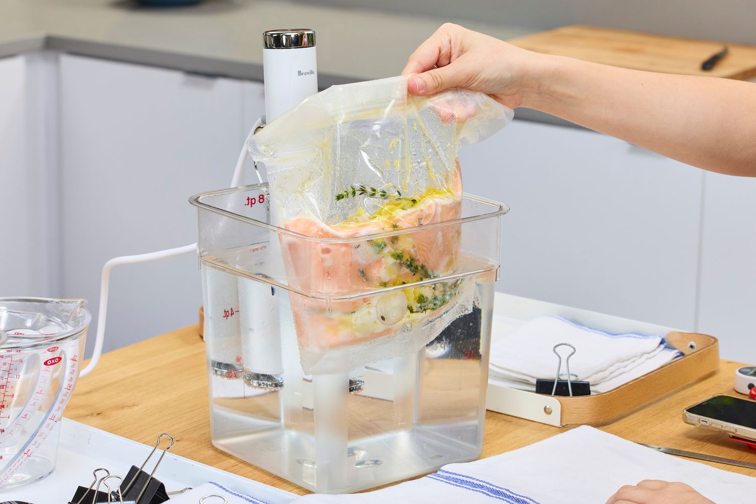 Hand placing a vacuum-sealed bag with food into a container of water to cook using the Breville Joule Turbo Sous Vide Machine