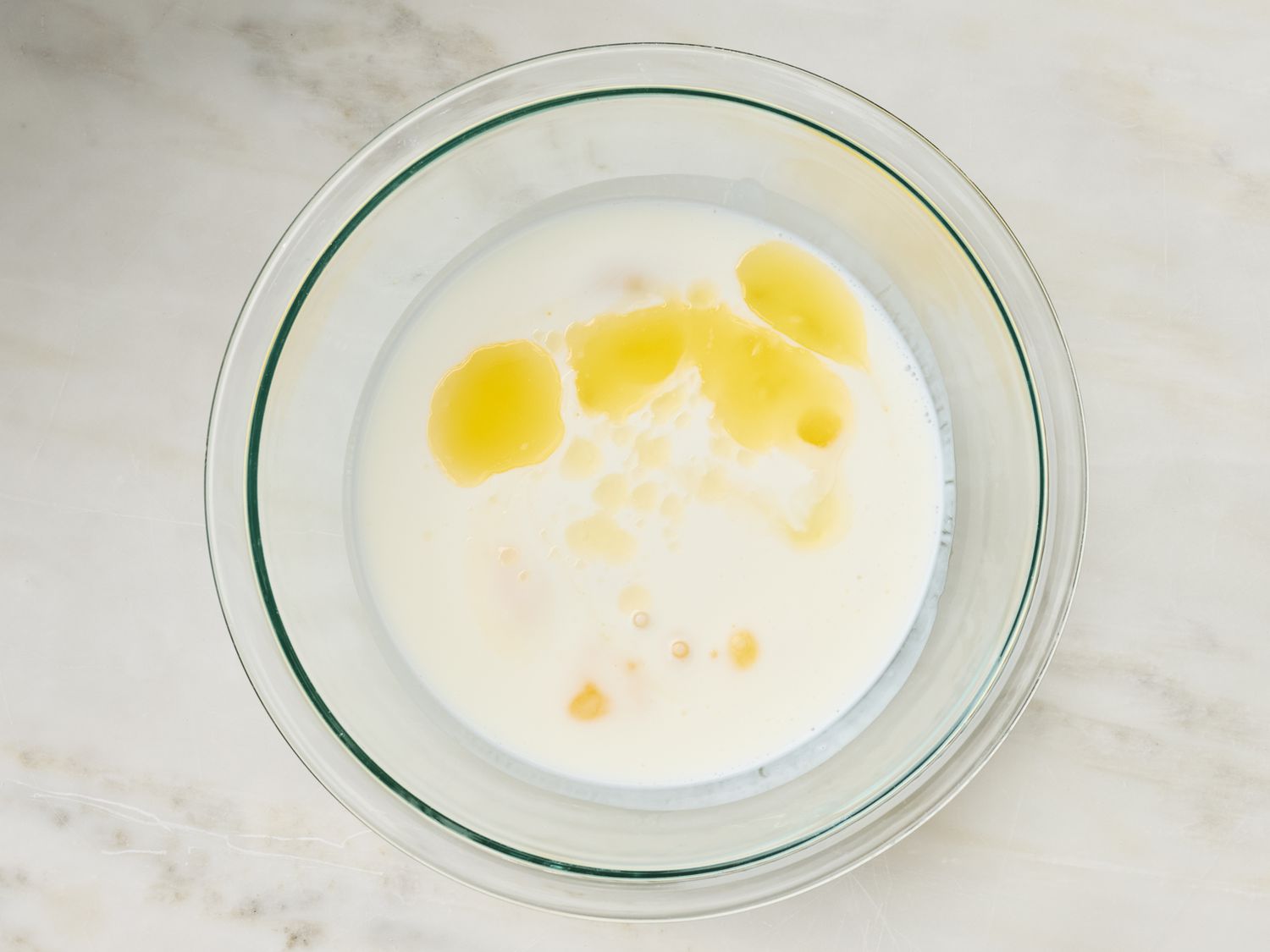 A glass bowl with milk and melted butter mixed in it, ingredients for preparing dough
