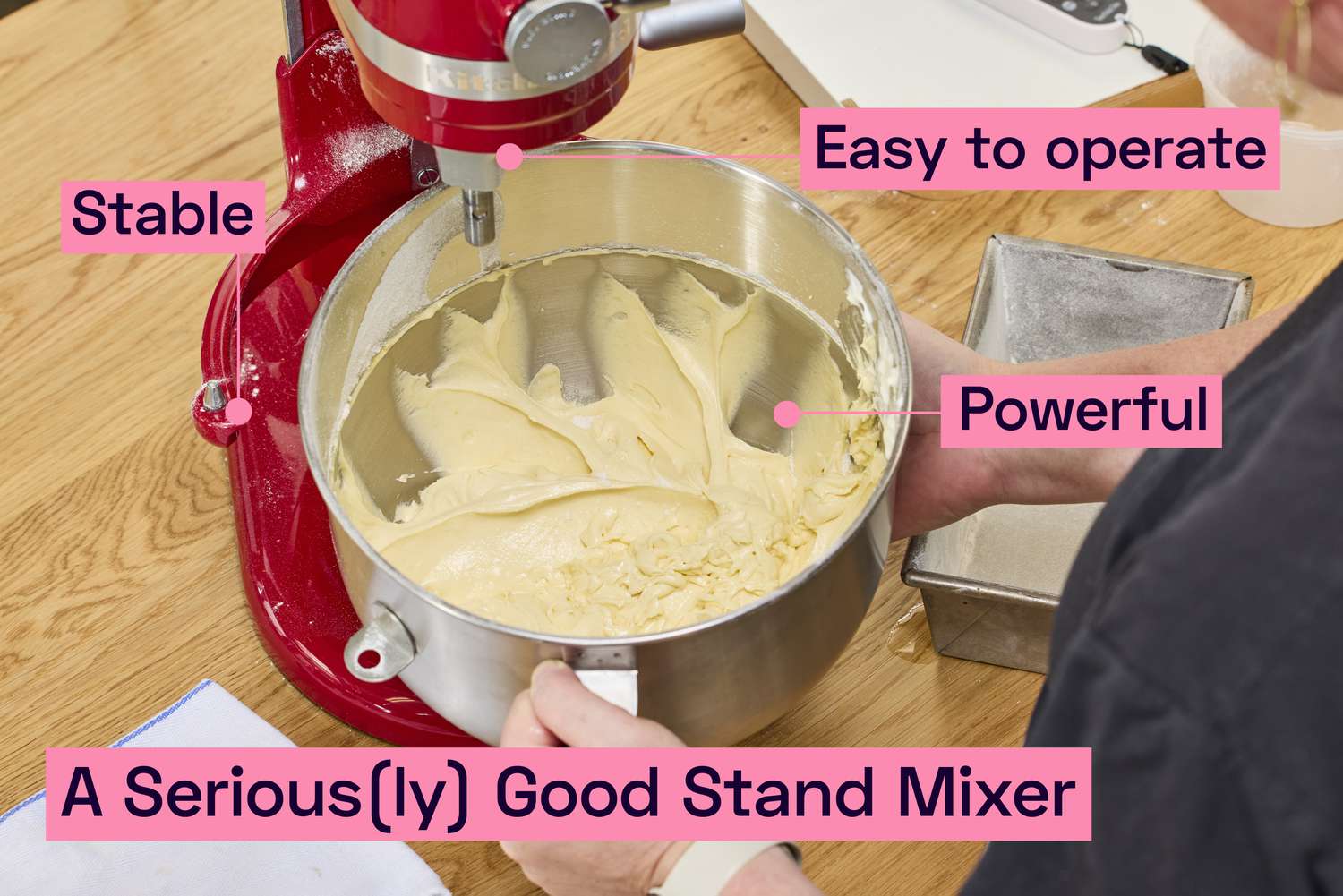 A person removing a bowl with batter in it from a stand mixer's base.