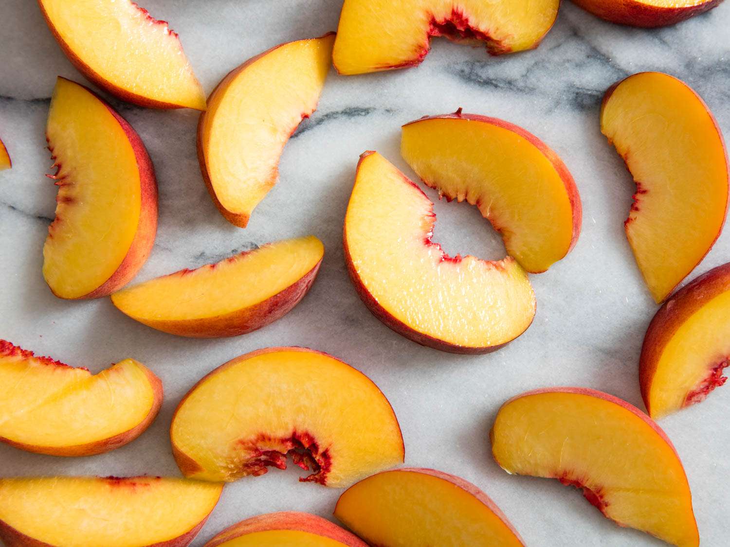 Overhead view of thick peach slices strewn across a white marble surface.