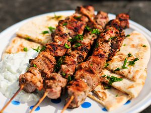 Three skewers of pork souvlaki on a plate with pita bread and tzatziki. 