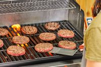 A person cooks meat in the Weber Genesis E-325 Liquid Propane Gas Grill