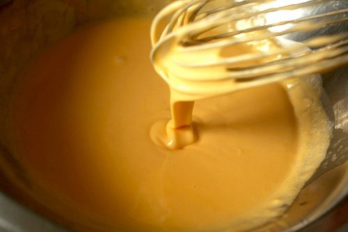 Smooth cheese sauce dripping off of a whisk into a bowl.