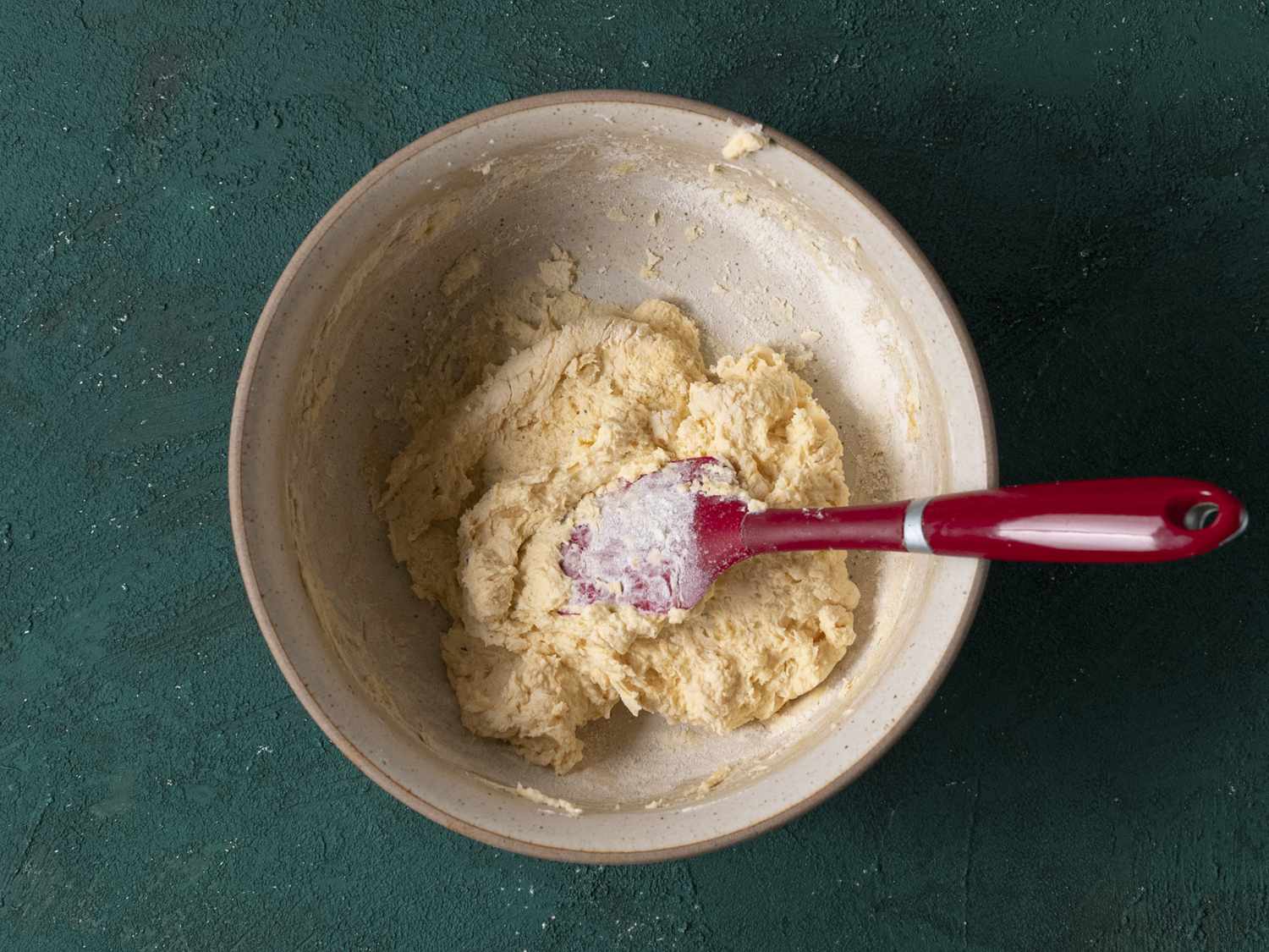 The sticky ricotta dough in a stoneware bowl with a red plastic spatula.