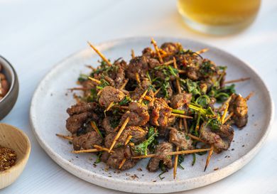 Plate of toothpick lamb set in front of out of focus glass of beer in background