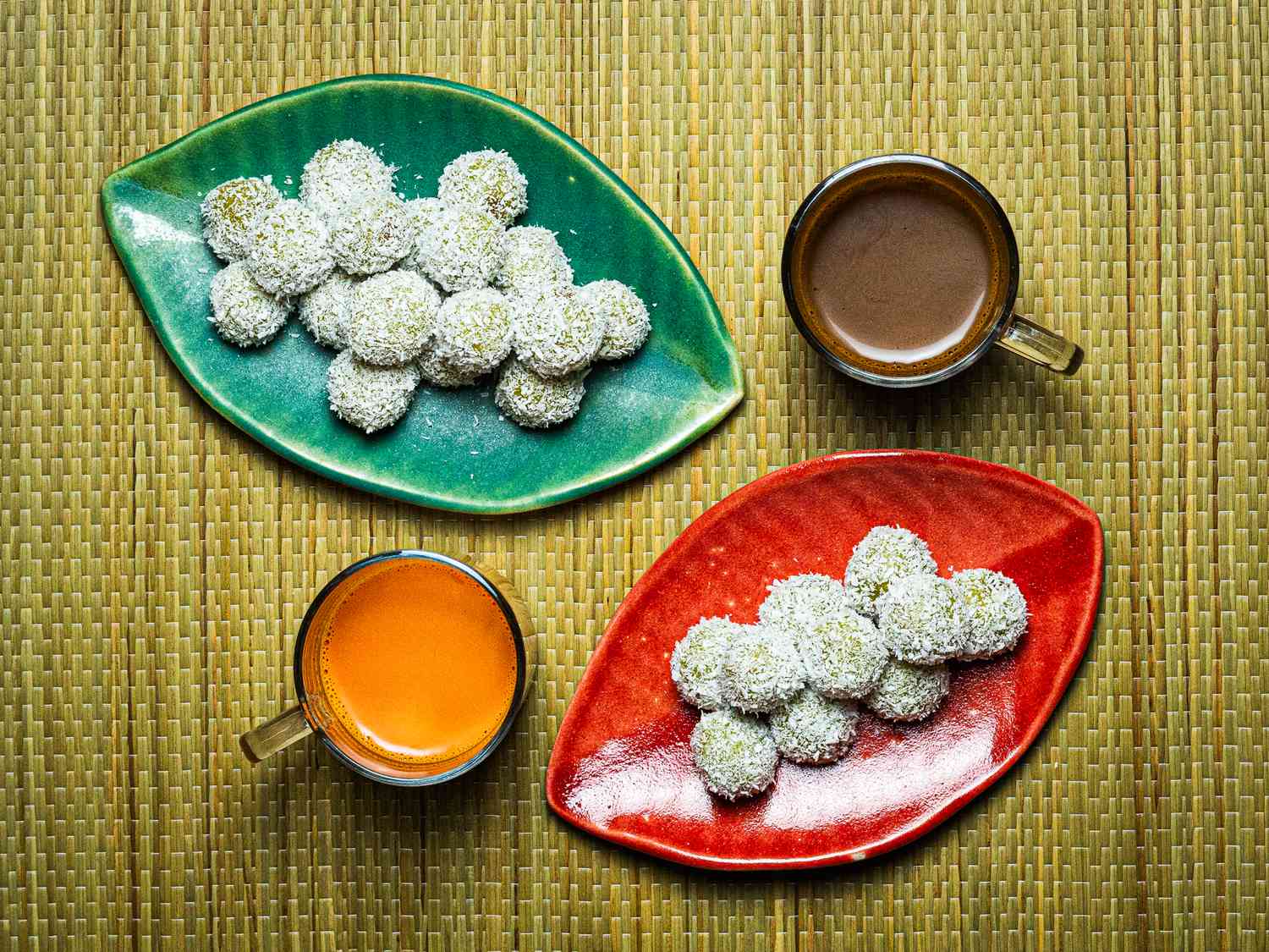 Overhead view of two plates of onde-onde with two drinks