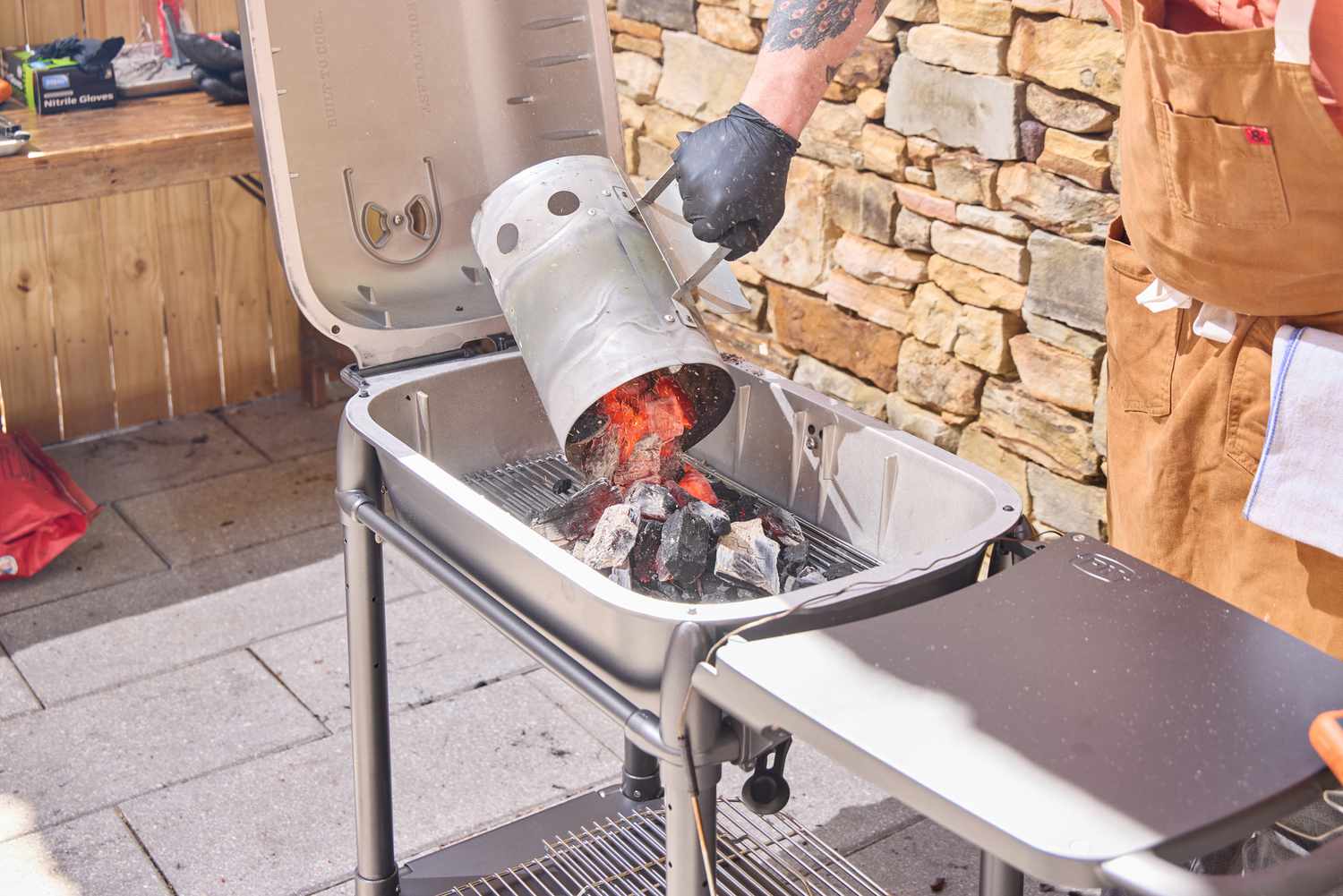 A hand adding hot coals to the PK Grills Original PK300 Grill & Smoker