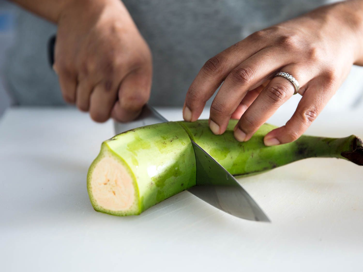 Cutting a green plantain with a chef's knife. 