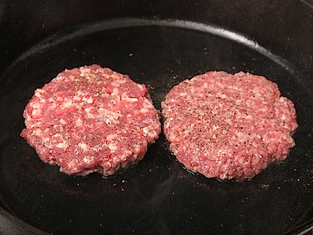 Coarsely and finely ground beef patties, cooking in a cast iron skillet.