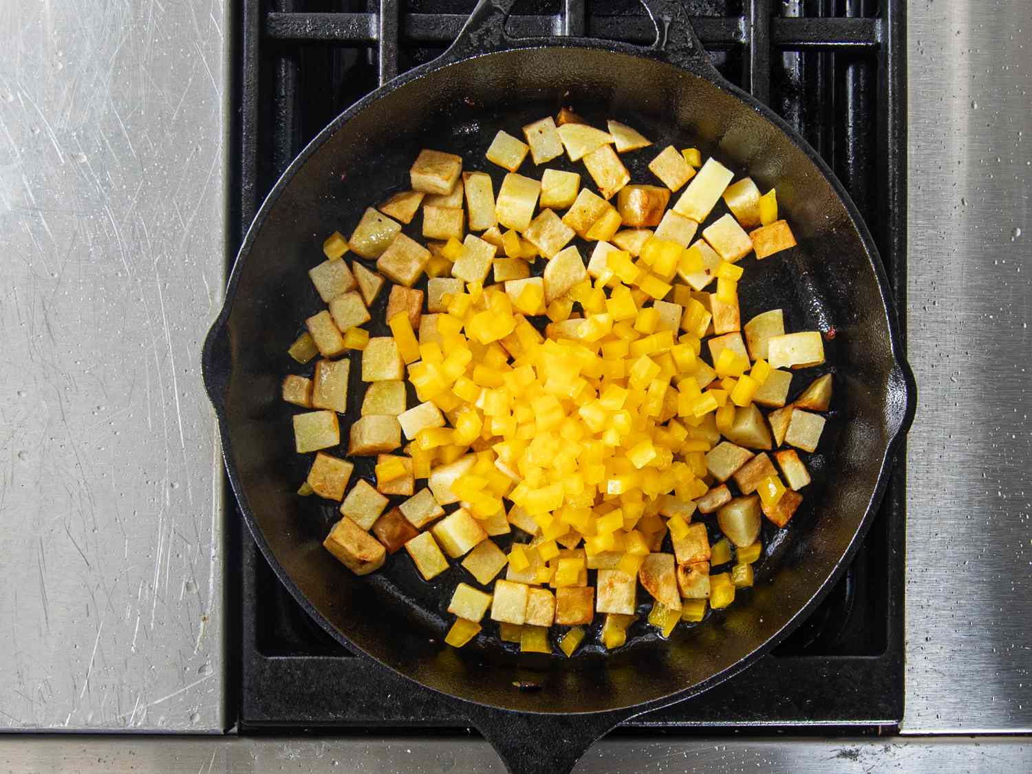 Dice yellow peppers on top of browned potatoes in cast iron skillet on stove
