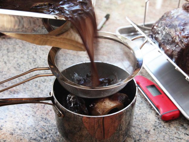 Straining red wine jus.