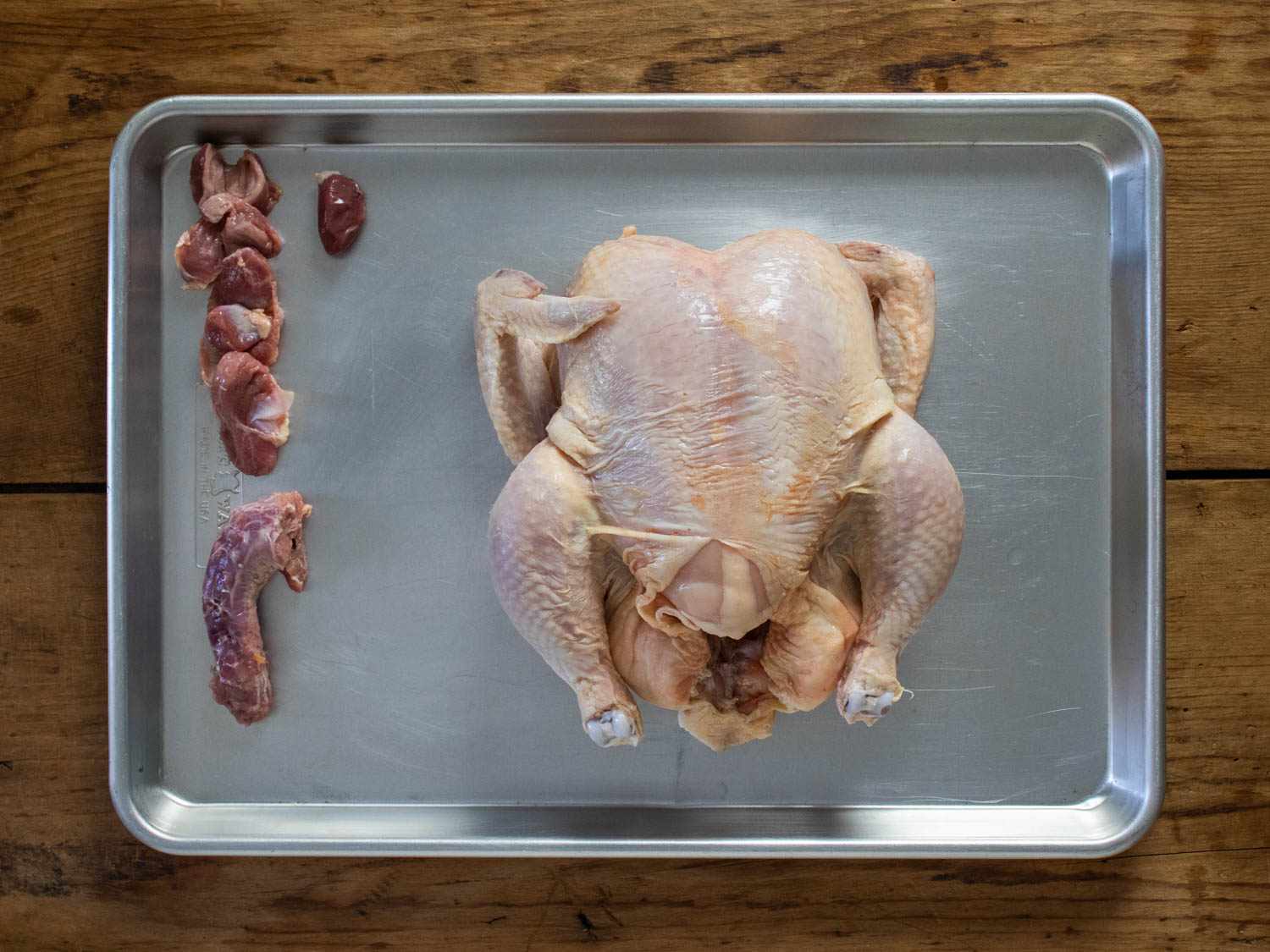 Whole chicken with its offal arranged next to it on a rimmed baking sheet.