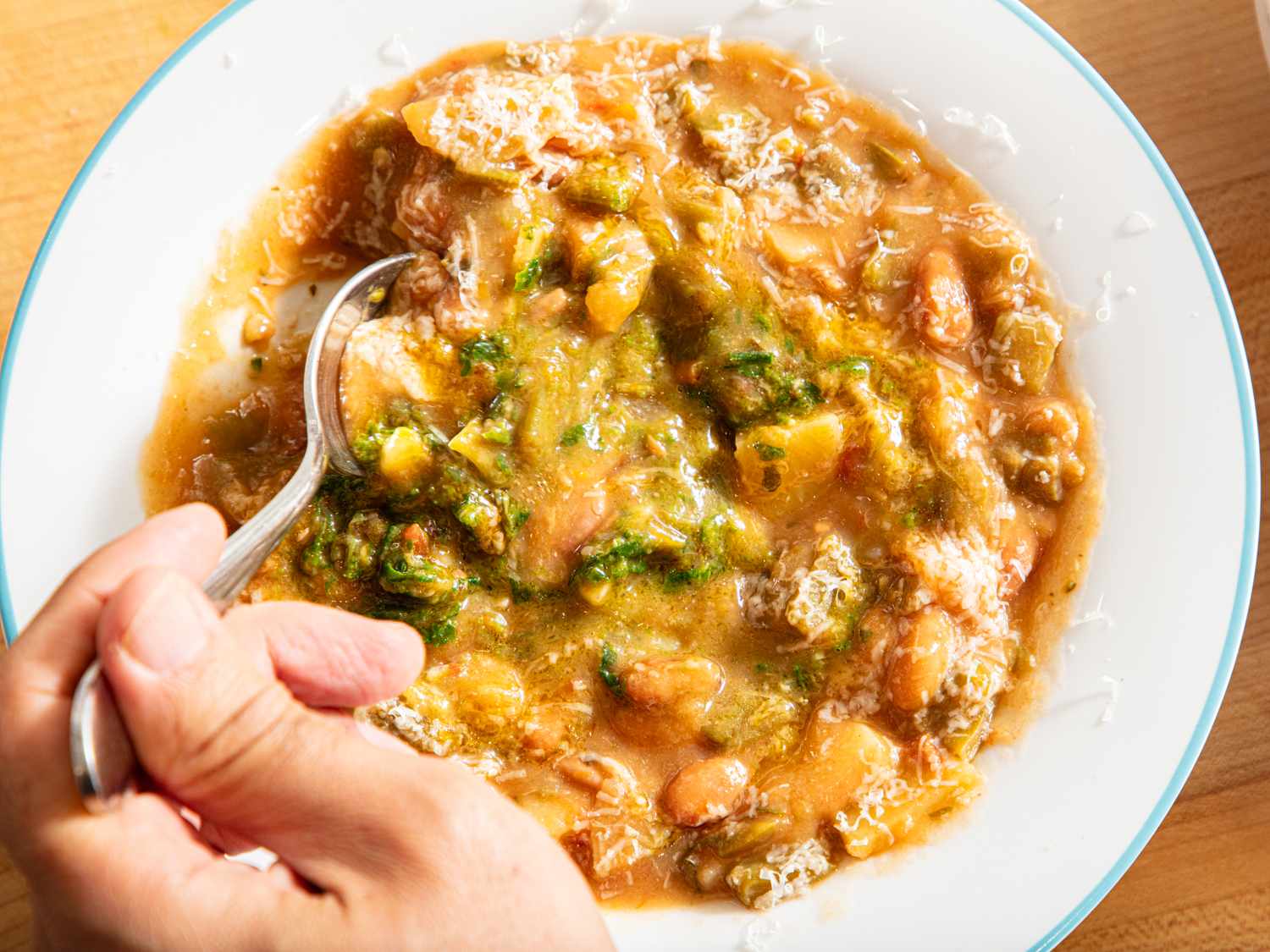 A hand holding a spoon over a bowl of hearty bean and vegetable stew