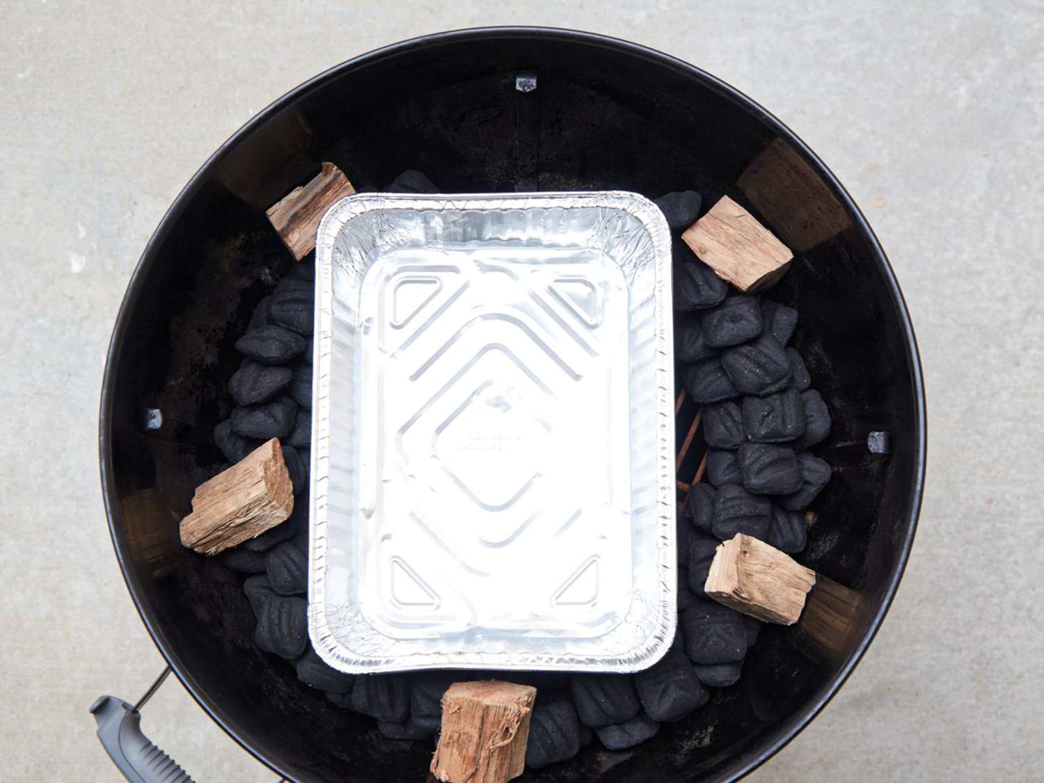 Outdoor smoker setup with charcoal, wood chunks, and a metal drip pan