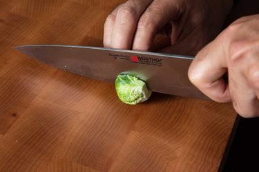 A trimmed Brussels sprout is sliced in half through the stem end with a chef's knife.