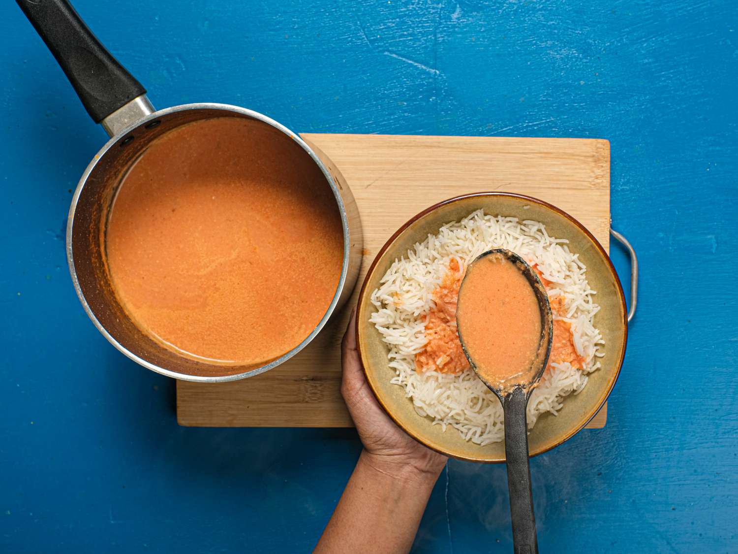 Spooning soup onto bowl of rice on wooden board
