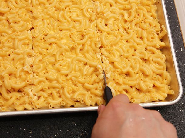 Cutting into a sheet pan of solid mac and cheese with a chef's knife.