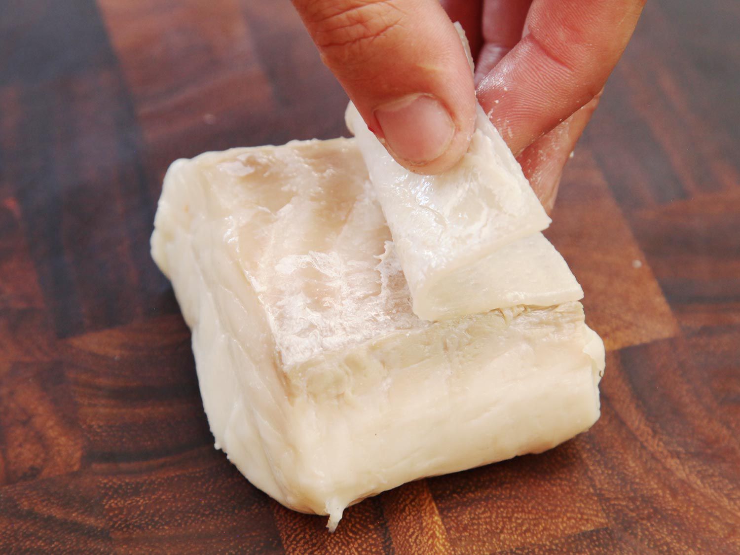 A hand removing skin from an uncooked square of halibut.
