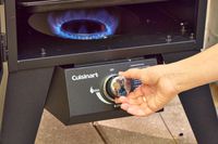 A person turns a dial on the Cuisinart COS-244 Vertical 36-inch Propane Smoker