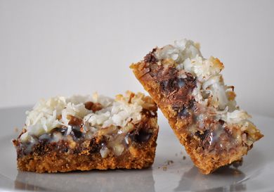 Two Hello Dolly bars with a graham cracker crust, chocolate chips, pecans, and toasted coconut on top. 