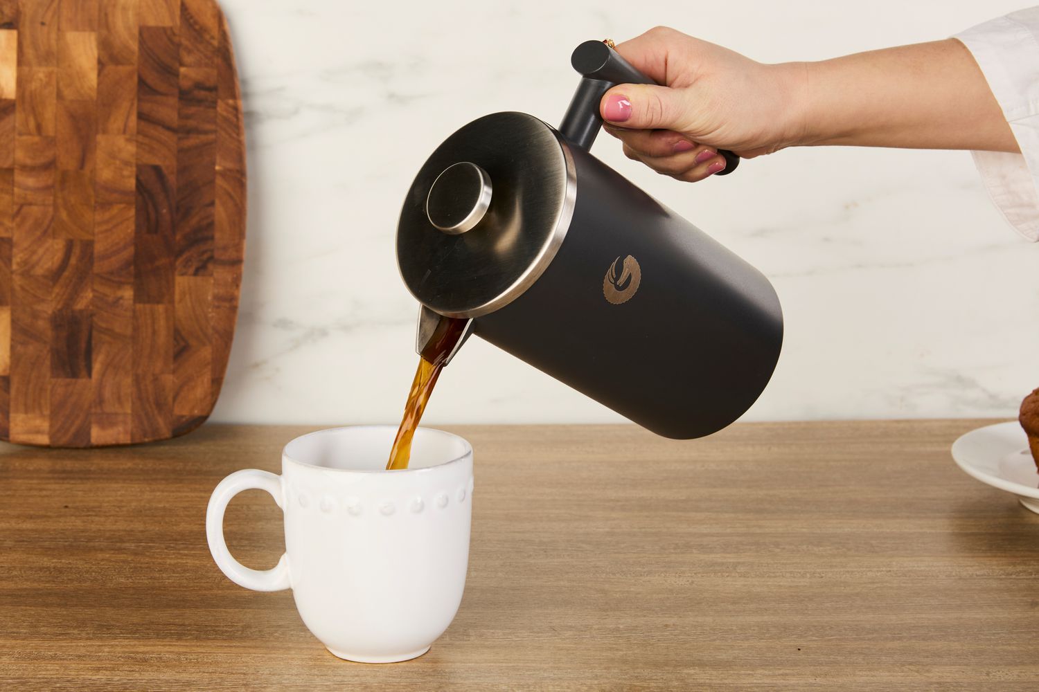 A person pouring coffee from a French press into a mug.