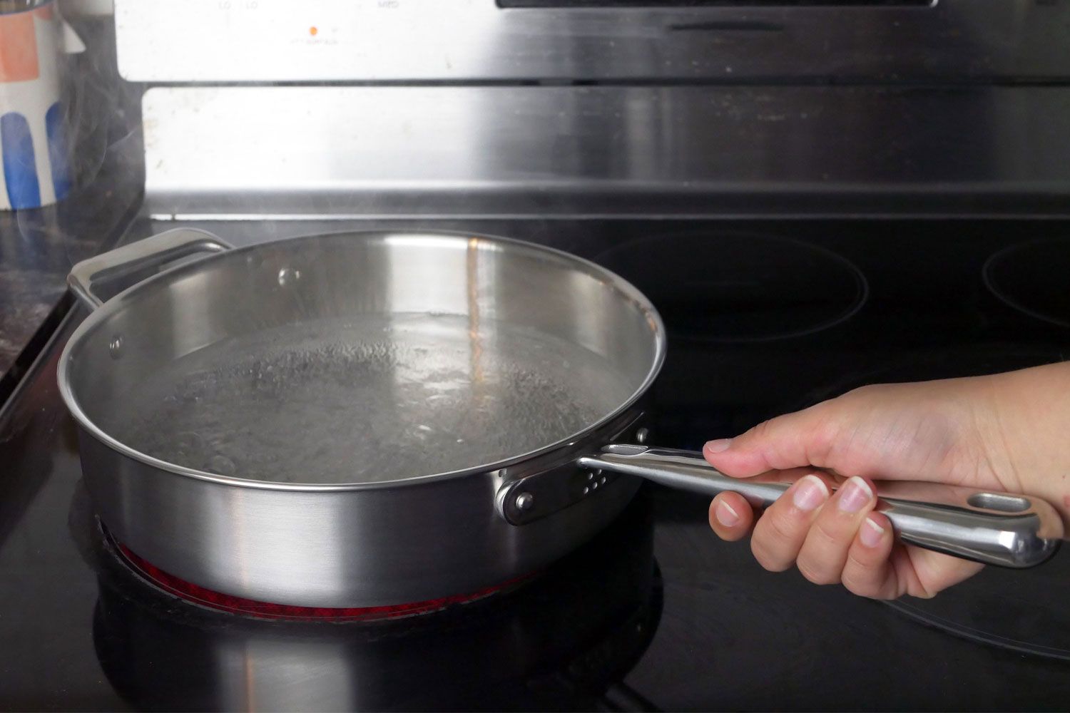 A hand holding the handle of the Misen 5 Ply Stainless Steel Saute Pan with boiling water