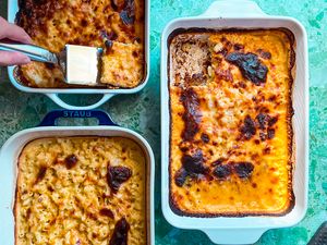 Three rectangular baking dishes of baked macaroni and cheese one with a slice being lifted with a spatula