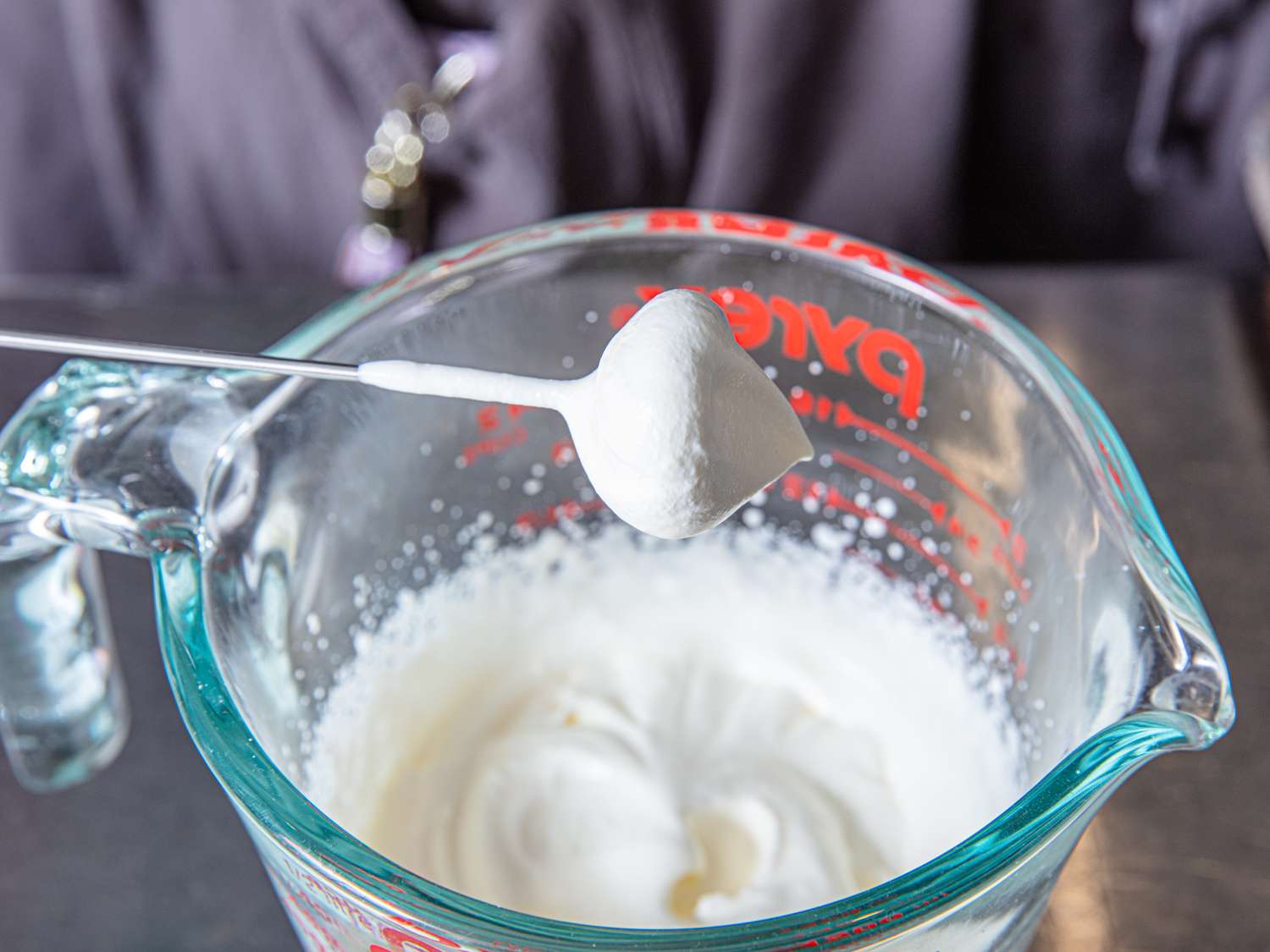 Measuring cup with frothy milk being scooped with a tool