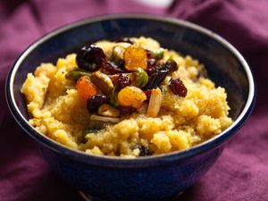 Bowl of semolina halva topped with spiced nuts and dried fruit