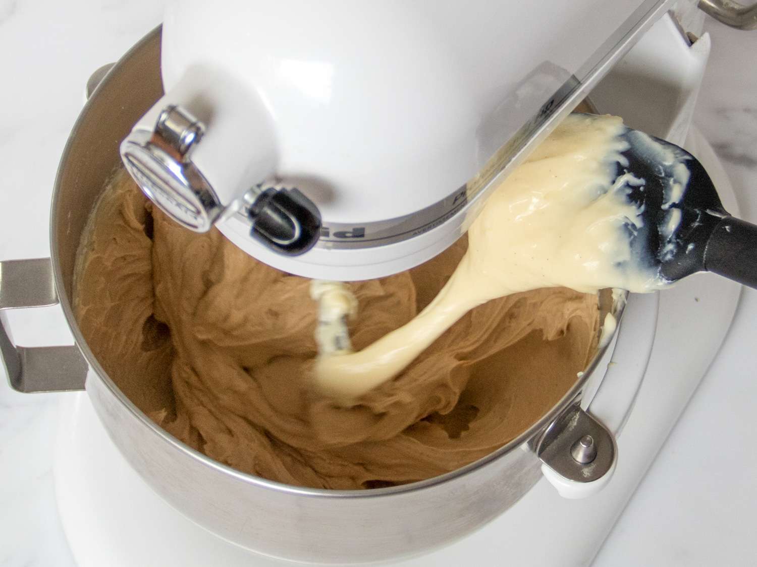 Pastry cream being added to the praline paste and butter mixer in the stand mixer.