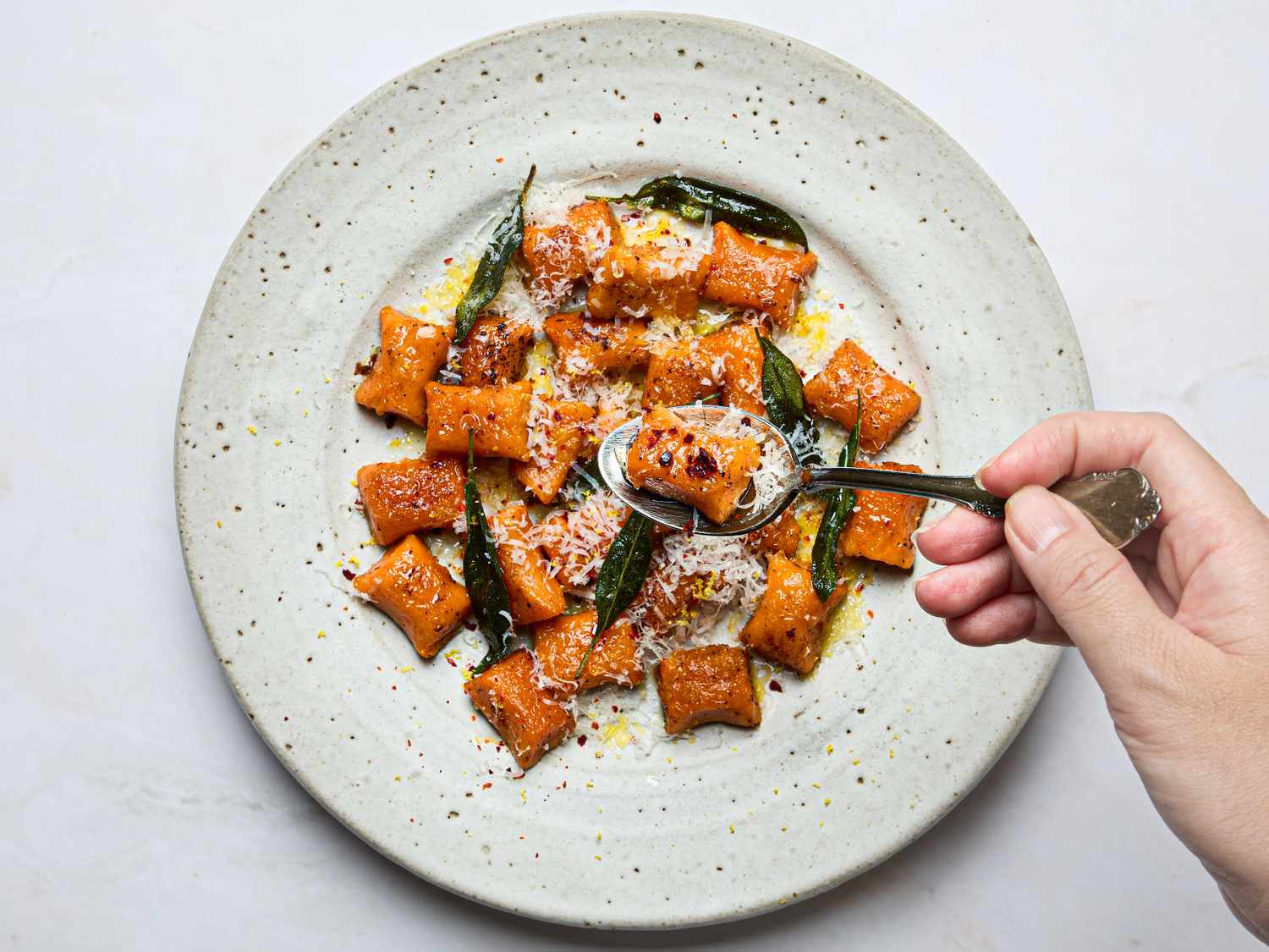 A plate of sweet potato gnocchi garnished with cheese and herbs with a hand holding a fork
