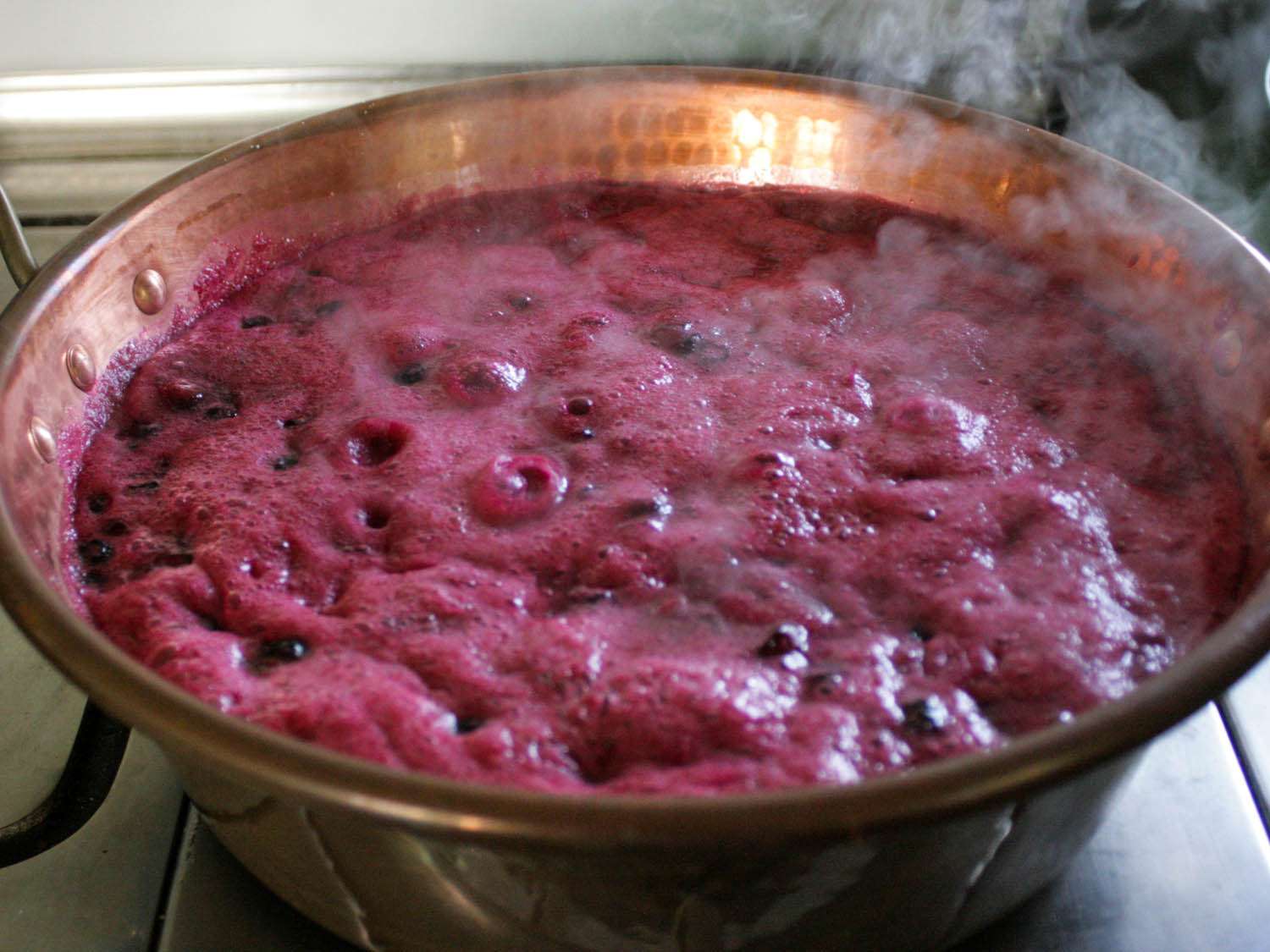 A copper pot filled with boiling blueberries and liquid.